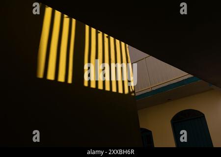 Sonnenlicht wirft dramatische Schatten auf eine gelbe Wand und erzeugt ein auffälliges geometrisches Muster Stockfoto