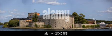 Ein Panoramablick auf eine historische Steinfestung (Waxholm), umgeben von Wasser, mit einem runden Turm und mehreren Gebäuden mit Bäumen im Vorland Stockfoto