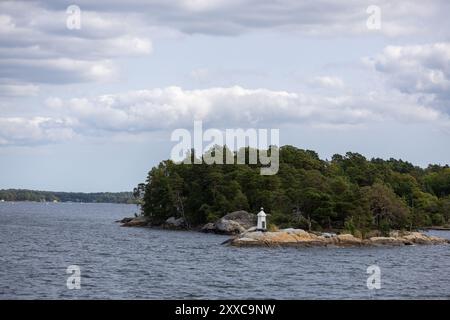 Eine ruhige Küstenszene mit einer kleinen Insel mit üppigen grünen Bäumen und einem weißen Leuchtturm. Das ruhige Wasser reflektiert den bewölkten Himmel und sorgt für Ruhe Stockfoto