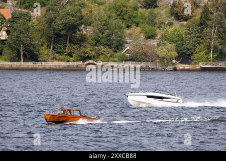 Zwei Boote auf einem ruhigen Gewässer, eines aus Holz und Vintage, das andere modern und elegant, umgeben von üppigem Grün und einer malerischen Küste. Stockfoto