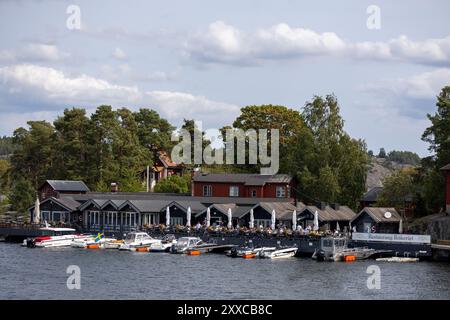 Ein malerisches Restaurant am Wasser mit Sitzgelegenheiten im Freien, umgeben von Bäumen und Booten, die am Ufer anlegen. Der Himmel ist teilweise bewölkt, was eine Ruhe schafft Stockfoto