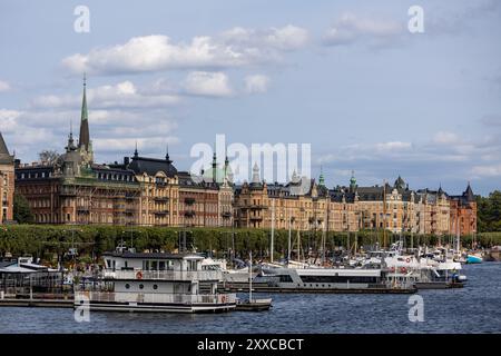 Ein malerischer Blick auf eine Uferpromenade in einer Stadt mit historischen Gebäuden mit kunstvoller Architektur, Booten im Vordergrund und einem bewölkten Himmel. Stockfoto