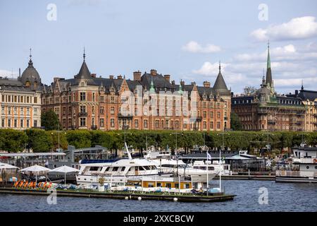 Ein malerischer Blick auf eine Uferpromenade in Stockholm mit historischen Backsteinhäusern mit Türmen und Türmen. Boote sind im Vordergrund angedockt, mit einer Clea Stockfoto