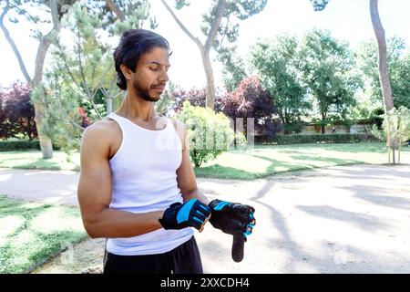 Ein Mann in einem weißen Tanktop und schwarzen Shorts trägt ein blaues Armband. Er steht in einem Park und konzentriert sich auf etwas Stockfoto