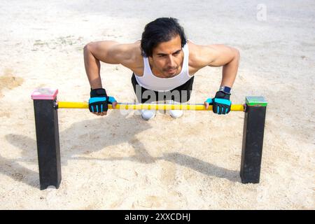 Ein Mann macht einen Push-up auf einer gelben Leiste. Er trägt ein weißes Tanktop und schwarze Shorts Stockfoto