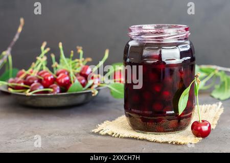 Sauerkirschmarmelade im Glas oder in einer Schüssel mit frischen, rohen Sauerkirschen Stockfoto