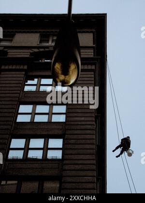 Ein Fensterreiniger, der zwischen Fenstern, die an einem Seil von einem Gebäude in der Washington Street und Water Street in DUMBO hängen, ausbalanciert. Stockfoto