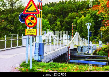 Blick auf die Brücke über den Fluss mit Straßenschildern umgeben von üppig grünen Bäumen und Herbstlaub im Vordergrund mit Schildern, die Einschränkungen und Warnungen anzeigen Stockfoto