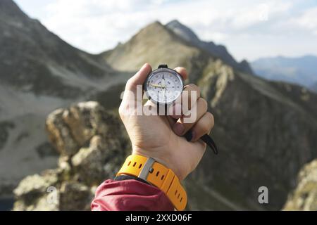 Die Hand eines Mannes hält einen magnetischen Taschenkompass für die Navigation vor dem Hintergrund eines felsigen Hanges und eines Berges. Das Konzept, einen Weg zu finden. Gainin Stockfoto