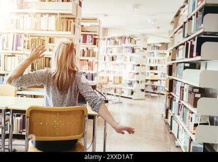 Müde Studentin sitzt am Schreibtisch mit einem Stapel Bücher, Universitätsbibliothek Stockfoto