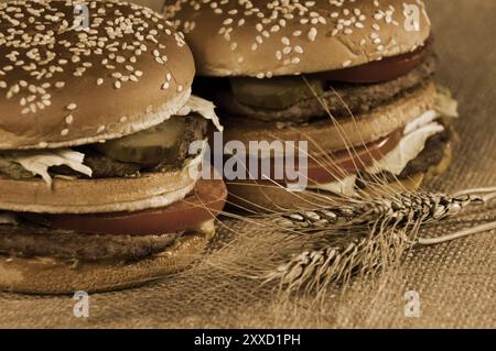 Zwei appetitliche Hamburger und Weizenohren zum Absacken. Ländliche Küche, Stillleben mit Sepia Stockfoto