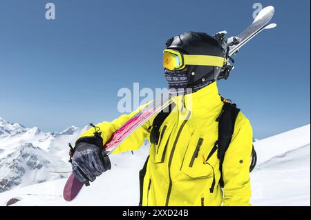 Ein großes Porträt eines Skifahrers in Schutzhelm und Brille ist eine Maske und ein Schal mit Skiern auf der Schulter in den schneebedeckten Bergen des Kauca Stockfoto