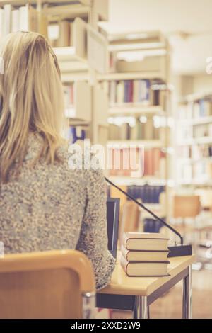 Blonde Studentin sitzt am Schreibtisch mit einem Stapel Bücher, Universitätsbibliothek Stockfoto