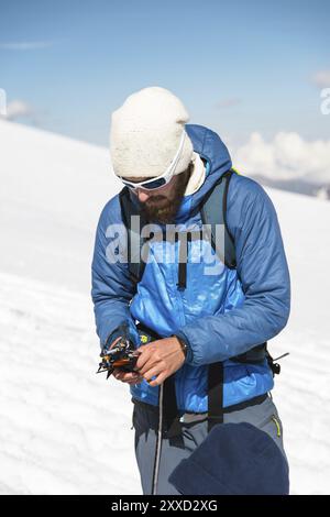 Ein junger Reiseleiter mit Bart und Sonnenbrille bereitet die Steigeisen für den Gebrauch vor Stockfoto