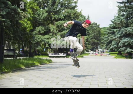 Der langhaarige Skater-Teenager in T-Shirt und Sneakermütze springt die ollie vor dem Hintergrund eines stürmischen Himmels durch die Stadt Stockfoto