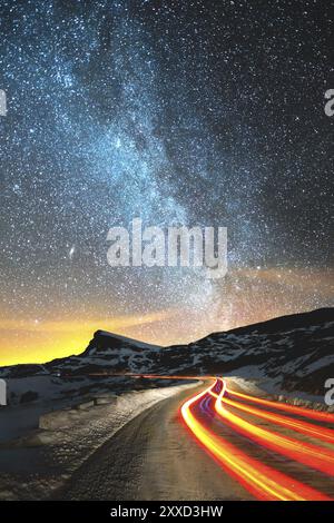 Nachtlandschaft. Nachthimmel mit einer Milchstraße auf der nördlichen Hemisphäre und Sternen. Die Nachtstraße, die vom Auto beleuchtet wird, windet sich mit einer Serpentine und fährt in A ab Stockfoto