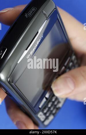 Strock-Foto einer Hand mit BlackBerry 8310 Curve Smartphone isoliert auf blauem Hintergrund Stockfoto