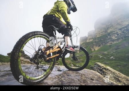 Beine des Radfahrers und Hinterrad Nahaufnahme des hinteren MTB-Bikes in den Bergen vor dem Hintergrund von Felsen bei nebeliger Witterung. Das Konzept der extremen spor Stockfoto