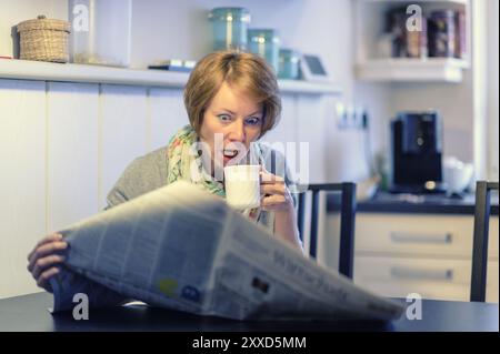 Die junge Frau sitzt am Küchentisch und liest die Zeitung entsetzt Stockfoto