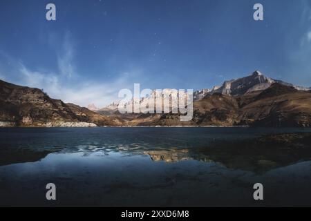 Nächtliche Landschaft prächtige kaukasische Felsen, die in der Ferne vor dem Hintergrund des Nachthimmels mit Wolken mit einem halbgefrorenen See an der verlassen Stockfoto