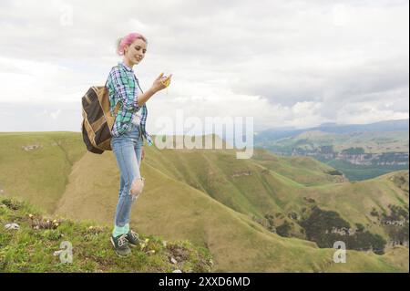 Ein Hipster-Mädchen reiste von einem Blogger in einem karierten Hemd und mit mehrfarbigen Haaren mit einem Kompass, der auf einem Hochplateau in den Bergen stand Stockfoto