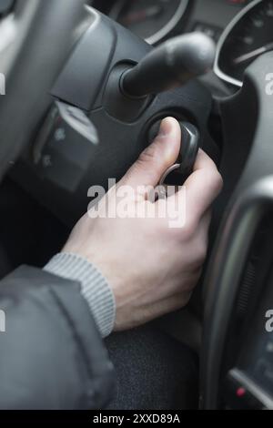 Nahaufnahme im Fahrzeug: Schlüssel in der Hand in der Zündung, Lenkrad und schwarzer Innenhintergrund, Fahrerkonzept männlich Stockfoto