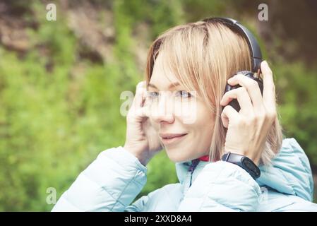 Nahaufnahme Porträt einer schönen jungen Frau mit Kopfhörern, die im Wald Musik hören. Fröhliche Musik Stockfoto