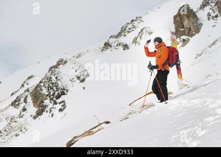 Ein Ski-Freerider, der auf einer Piste in einem tiefen Schneepulver steht, fotografiert die Landschaft auf seinem Handy mit Ausrüstung auf dem Rücken, fixiert auf einem Backp Stockfoto