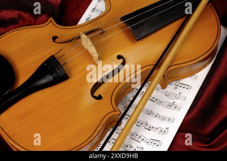 Violine und Noten auf rotem Hintergrund musikalisches Stillleben Stockfoto