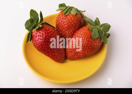 Drei Erdbeeren auf gelbem Schild. Auf einem weißen Hintergrund isoliert Stockfoto