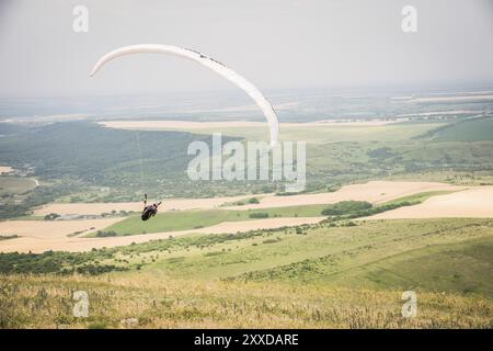 Weiß orange Gleitschirm mit einem Gleitschirm in einem Kokon vor dem Hintergrund von Feldern des Himmels und Wolken. Paragliding Sport Stockfoto