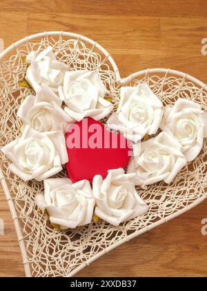 Herzförmige Schüssel mit weißen Rosen und roten Geschenk-box Stockfoto