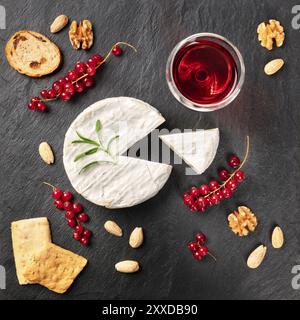 Ein Foto von Camembert mit einem Glas Rotwein, Obst und Nüsse, Schuß von oben auf einem schwarzen Hintergrund mit Kopie Raum Stockfoto