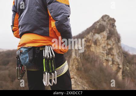 Nahaufnahme eines Oberschenkelkletters mit Ausrüstung auf einem Gürtel, steht auf einem Felsen auf einem Hügel Hintergrund Stockfoto