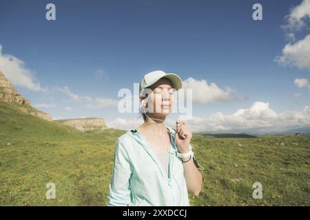 Fitness-Läuferin schließt die Augen und hört Musik über die Natur. Porträt eines schönen Mädchens mit Ohrhörern und Laufkappe. Nein Stockfoto