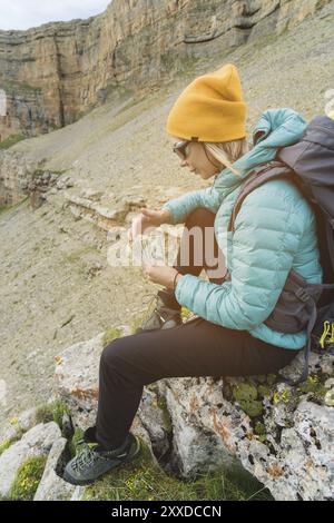 Ein Reisemädchen mit Hut und Sonnenbrille hält hundert Dollar Scheine in den Händen eines Fans vor dem Hintergrund der Klippen in der Natur. Behalten Sie Ihr HE Stockfoto