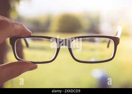 Junger Mann hält seine Brille im Freien, verschwommener Hintergrund Stockfoto