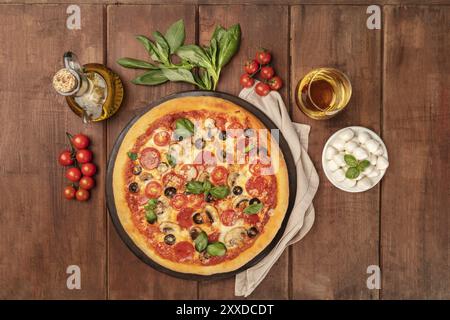 Ein Foto von einem Pepperoni Pizza mit einem Glas Weißwein, Olivenöl, Basilikum, Tomaten und Käse mozzarellini, Schuß von oben o Stockfoto