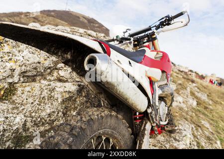 Details zum Enduro-Motorrad. Weitwinkel. Der Heckflügel mit einem Auspuffrohr und einem Rad auf dem Hintergrund des Fels und des Himmels Stockfoto