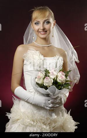 Junge schöne Braut in einem Hochzeitskleid mit einem Haufen weißer Rosen auf dunkelrot Stockfoto