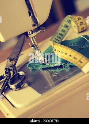 Nahaufnahme einer Nähmaschine mit grünem Stoff und Nähutensilien, selektiver Fokus, Retro-Farbton Stockfoto