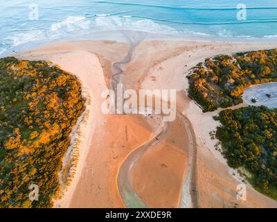 Aus der Vogelperspektive auf einen Küstenbach, der sich über den Strand und ins Meer schlängelt, bei Anglesea an der Great Ocean Road in Victoria, Australien. Stockfoto