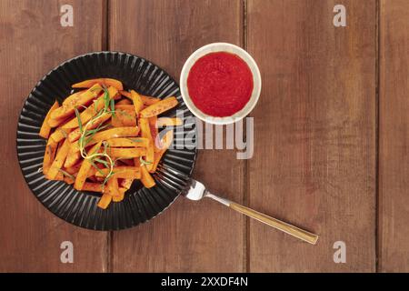 Süßkartoffel frites mit Rosmarin und Ketchup, geschossen von oben auf einen dunklen Holzmöbeln im Landhausstil Hintergrund mit einer Gabel und Kopie Raum Stockfoto