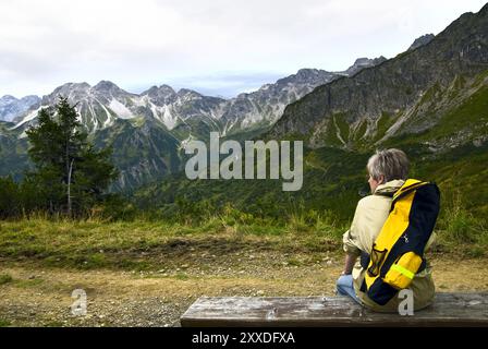 Frau, die auf einer Bank sitzt und die Berge ansieht Stockfoto