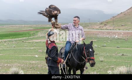 Issyk Kul, Kirgisistan - 23. Mai 2022: Adlertrainer hilft einem Touristen, einen goldenen Adler zu halten, ein Erlebnis-Urlaub Stockfoto