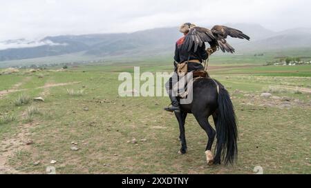 Issyk Kul, Kirgisistan - 23. Mai 2022: Adlertrainer zu Pferd mit seinem goldenen Adler, der traditionelle Jagdtechniken zeigt, die durch g übertragen wurden Stockfoto