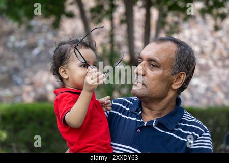 Enkel spielt mit Großvaters Brille in der Abenddämmerung in Park Stockfoto