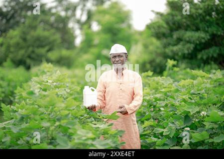 Glücklicher Bauer im indischen Dorf, der eine Düngemittelflasche hält, indem er vor die Kamera auf das Ackerland schaut - Konzept der Produktwerbung, Empfehlung und Landwirtschaft Stockfoto