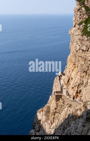 Große Klippe mit nicht erkennbaren Leuten, die durch einen Korridor laufen, der in der Mitte der Klippe über einem blauen Meer gegraben wurde. Naturlandschaft auf Sardinien Stockfoto