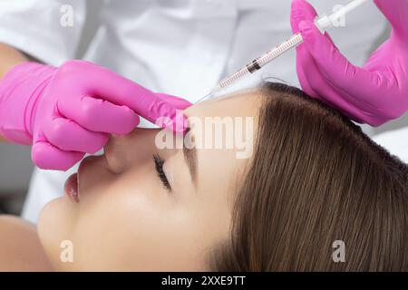 Frau bei der Kosmetikerin. Der Kosmetiker führt Antifalteninjektionen auf die Stirn und zwischen die Augenbrauen durch. Frauenkosmetologie im Schönheitssalon. Stockfoto